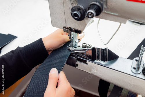 Close-up of a person sewing heavy fabric on an industrial sewing machine. The needle, presser foot, and hands are shown working on a piece of textile in a workshop. Shoe sewing machine, cylindrical.