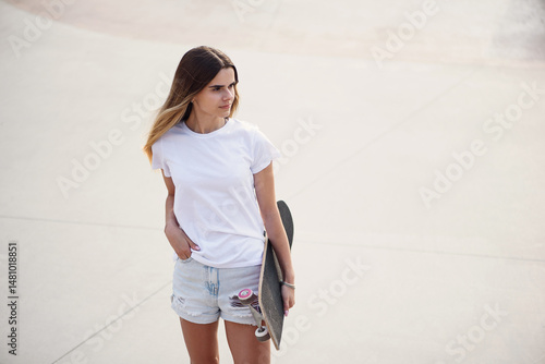 Young pretty girl in a white t-shirt and denim shorts holding skateboard.