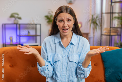 What. Why. Frustrated Caucasian young woman raising hands in indignant expression, asking reason of failure, demonstrating disbelief irritation by troubles, quarrel sitting on home couch. Girl at room
