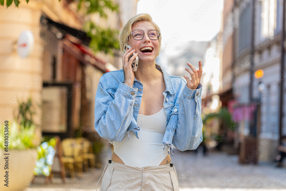 Fototapeta premium Phone call, good news, gossip. Happy Caucasian young woman in pleasant conversation on smartphone, enjoying talking with friend outdoors. Girl in trendy clothes on urban city street. Town lifestyles.