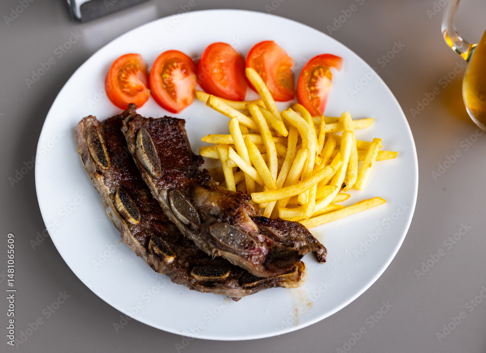Spanish cuisine. Delicious grilled beef ribs with a side dish of fresh tomatoes and fried potatoes