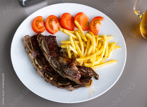 Obraz na płótnie Spanish cuisine. Delicious grilled beef ribs with a side dish of fresh tomatoes and fried potatoes w salonie