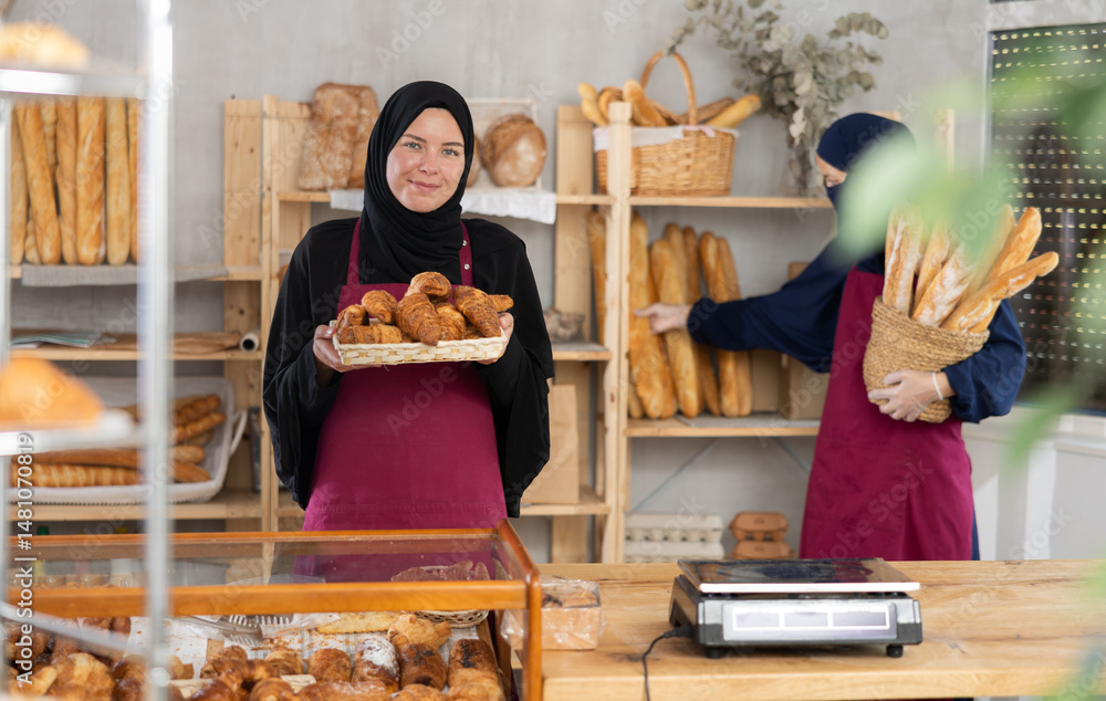 Girl seller of an oriental bakery in traditional muslim clothes with fresh hot croissants in her hands