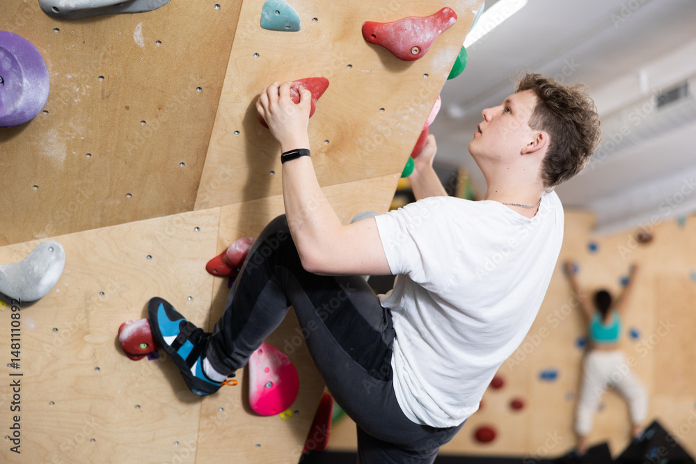 Teenage boy visitor to fitness club clambs wall for amateur climbers, side view. Active recreation, hobbies, recreation for active and sporty people