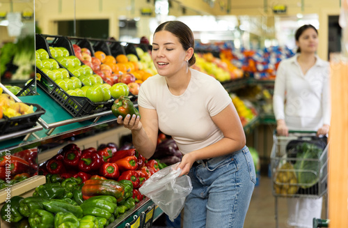 Obraz na płótnie Young woman shopper in casual clothes chooses bell pepper in supermarket w salonie