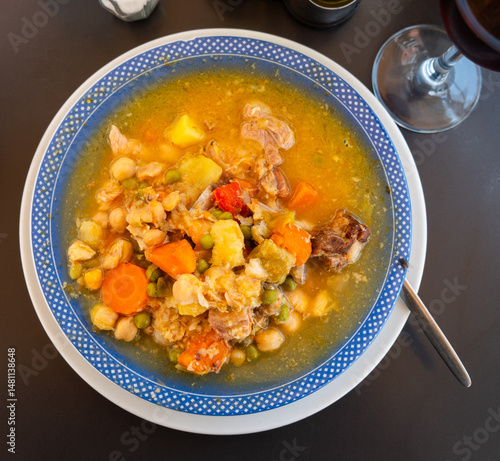 Plate with portion of hot chickpea and meat soup. First course is served with pieces of baguette..