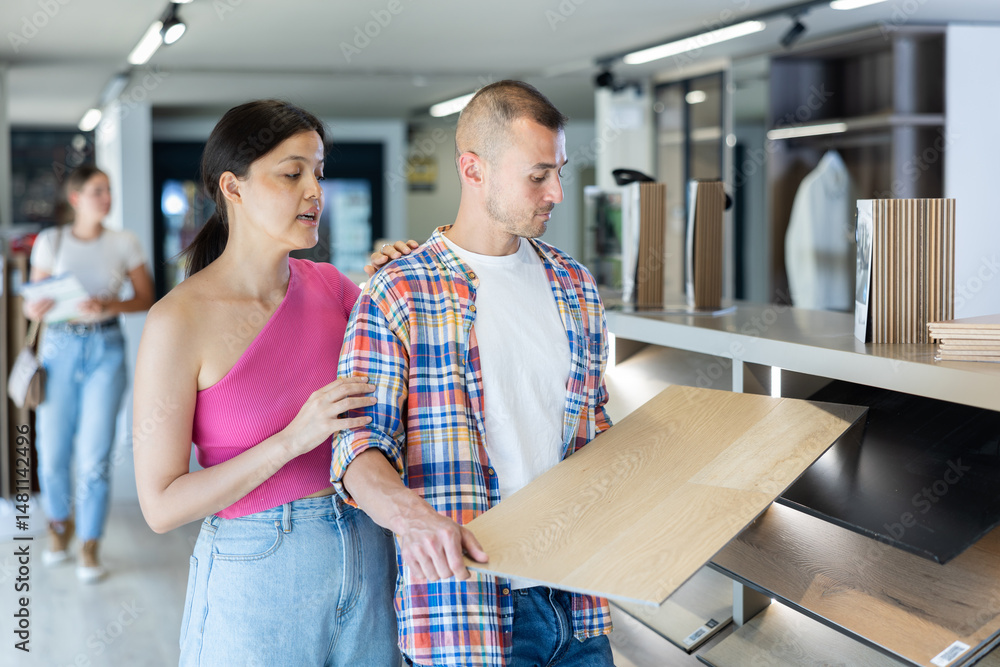 Couple of young man and woman choosing sample of laminate flooring in hardware store