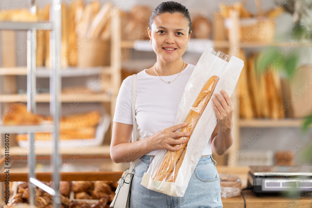 Glad middle-aged woman holds bag containing some baguettes just bought in bakehouse