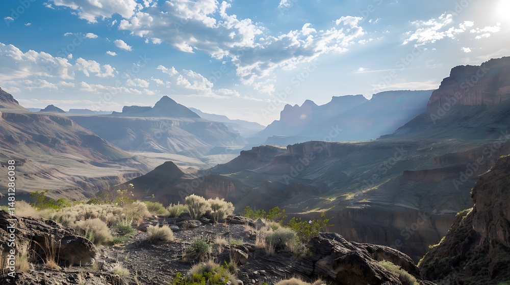 Obraz premium Vast Canyon Landscape Under Blue Sky with Golden Sunlight Shining Through Clouds