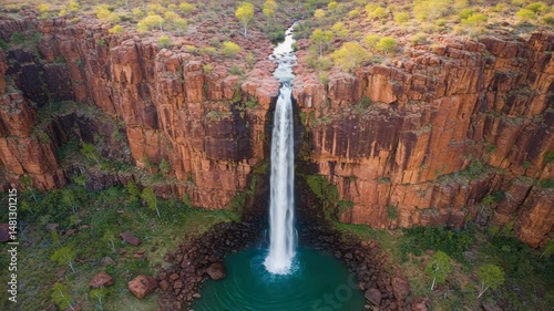 Aerial view of a waterfall flowing into a pool in a rugged, rocky canyon.