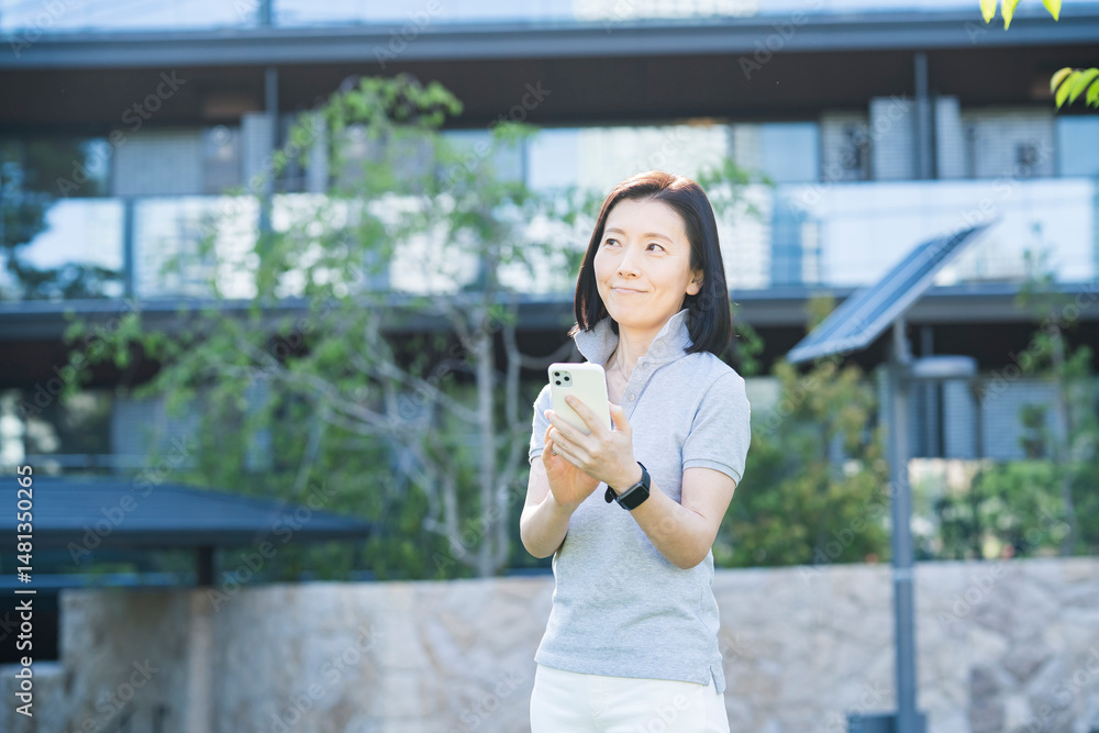 屋外でスマートフォンを操作する中年女性 屋外でスマートフォンを操作する中年女性