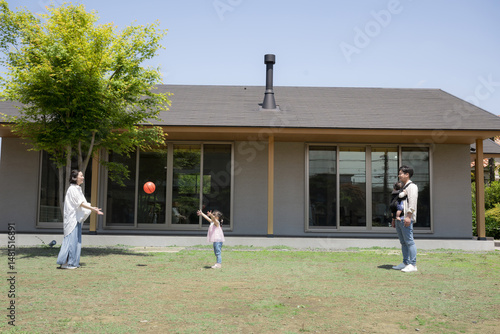 Family image of a happy estate of a family and children playing with a ball in front of the garden of a single-story detached house.