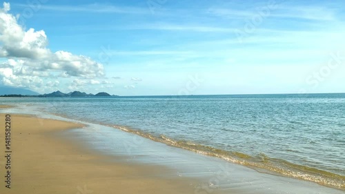 The atmosphere of the beach in the morning with green sea water, blue sky, mountains in the background and waves hitting the beautiful sandy beach. The atmosphere is very peaceful and refreshing