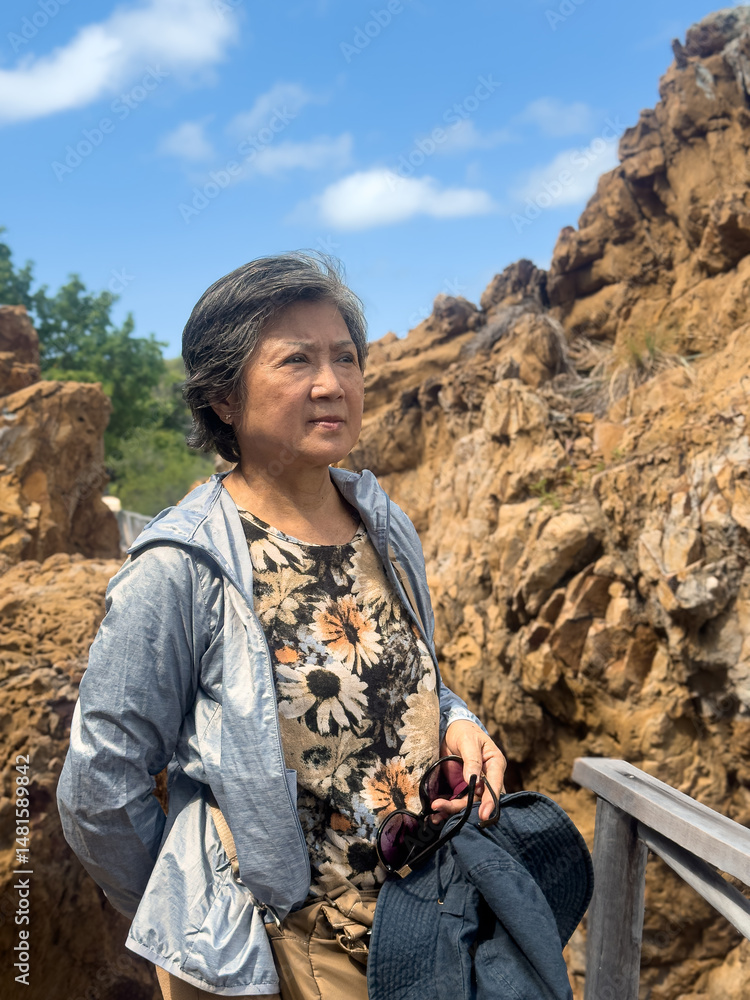Naklejka premium Happy asian Thai elder woman standing in front of beautiful rock and beach view in Thailand.