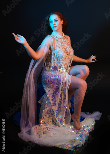 Fantasy studio portrait of a red-haired mermaid faery model wearing a white pearl gown, fairytale costume. posing in a classical sitting position with flowing fabric and ethereal moody studio lighting