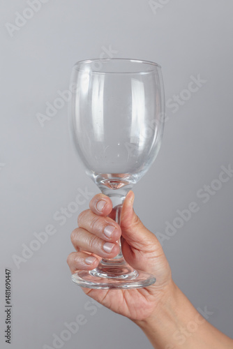 Hand holding empty wine glass by the base with fingers wrapped around clear transparent stemware for drinking or celebration themes on neutral background