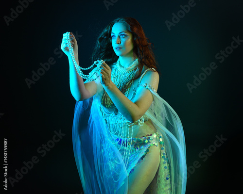 Fantasy studio portrait of a red-haired mermaid faery model wearing white pearl gown, fairytale costume. classical pose holding treasure, with flowing fabric, ethereal moody studio lighting