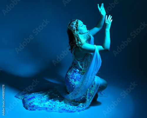 Fantasy studio portrait of a red-haired mermaid faery model wearing white pearl gown, fairytale costume. classical sitting pose,, ethereal moody blue lighting as if underwater on studio background