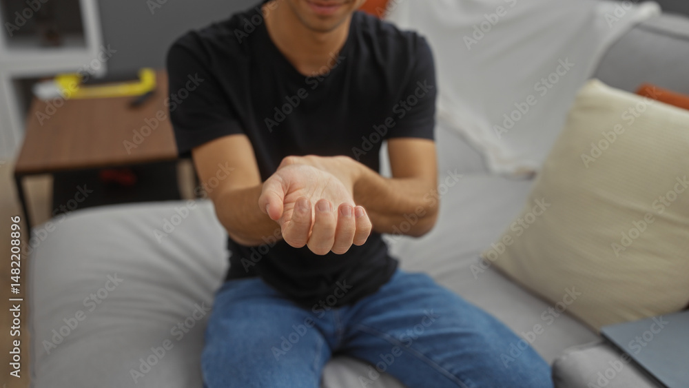 Young man indoors holding wrist in pain while sitting on a comfortable sofa in a modern living room interior apartment, suggesting discomfort or possible injury at home. Young man indoors holding wrist in pain while sitting on a comfortable sofa in a modern living room interior apartment, suggesting discomfort or possible injury at home.