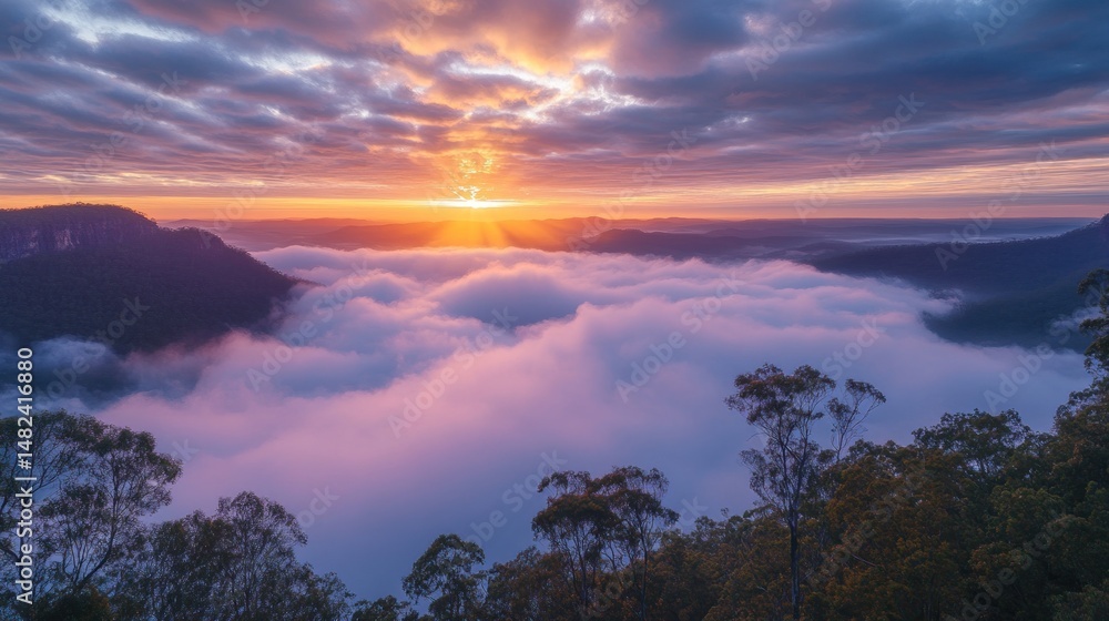 Obraz premium Sunrise over a valley shrouded in clouds, with vibrant colors, mountain ranges, and trees in the foreground..