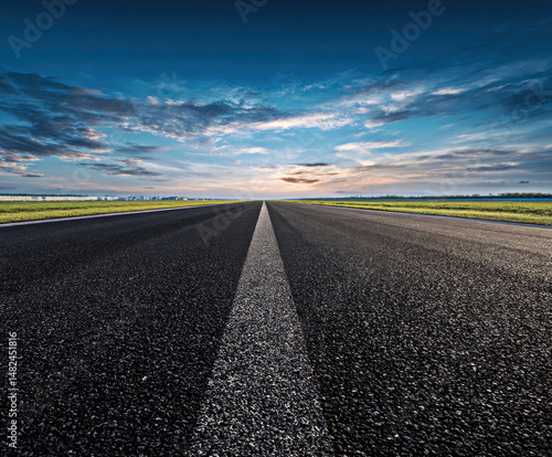 Obraz na płótnie This stunning image captures a wide, empty road stretching towards a vibrant horizon, revealing a breathtaking sky filled with dynamic clouds and hues of blue and orange. w salonie