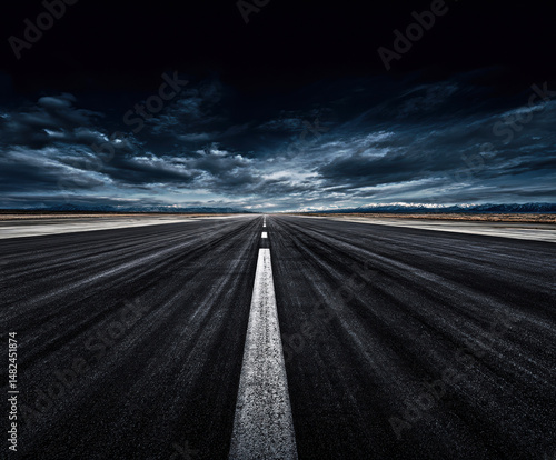 Obraz na płótnie A captivating view of a deserted runway stretching into the horizon, framed by dramatic clouds and distant mountains, evoking feelings of adventure and exploration. w salonie