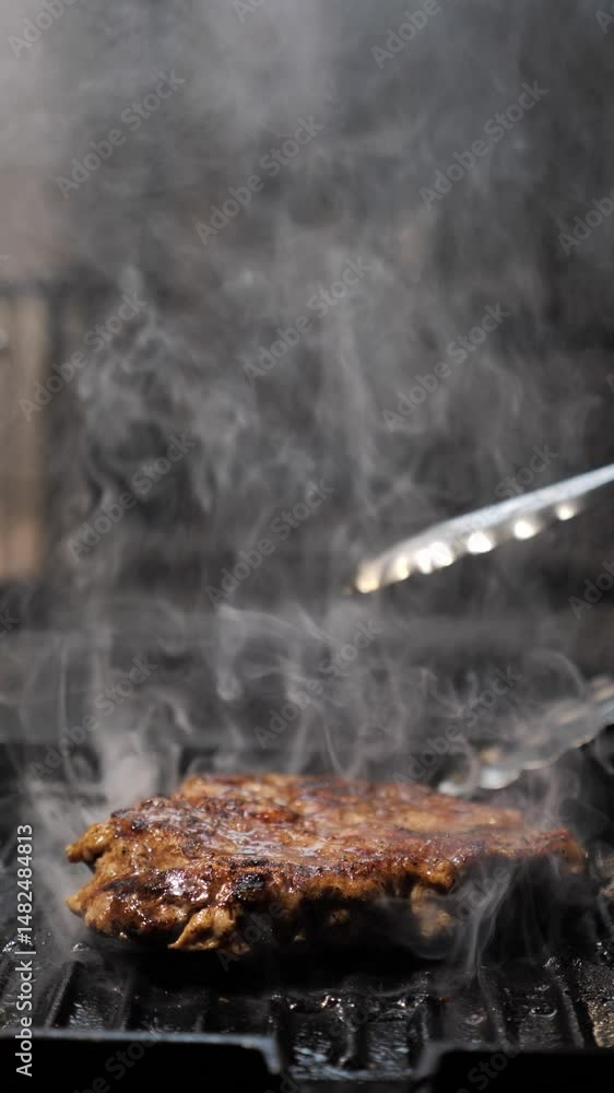 The chef flips the delicious steak with culinary tongs in a frying pan. frying juicy meat dish. Cooking in a restaurant. Vertical shots. Slow motion The chef flips the delicious steak with culinary tongs in a frying pan. frying juicy meat dish. Cooking in a restaurant. Vertical shots. Slow motion