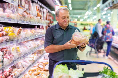 Elderly man chooses chicken meat in supermarket