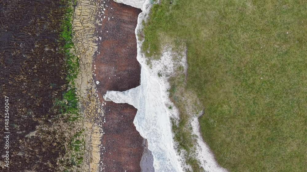 Overhead view of dramatic coastal cliffs meeting layered beach textures Overhead view of dramatic coastal cliffs meeting layered beach textures