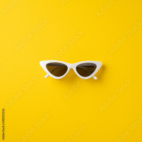 Stylish square white cat-eye sunglasses isolated against a vibrant yellow background emphasizing summer fashion vibes