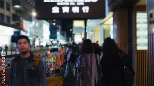 Pedestrians leisurely stroll through the neon-lit streets of Hong Kong at night, capturing the dynamic urban atmosphere and distinctive signage. A glimpse of nightlife in the city