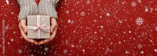 Holiday Gift Held in Hand With Falling Snow Against Bright Red Background in ...
