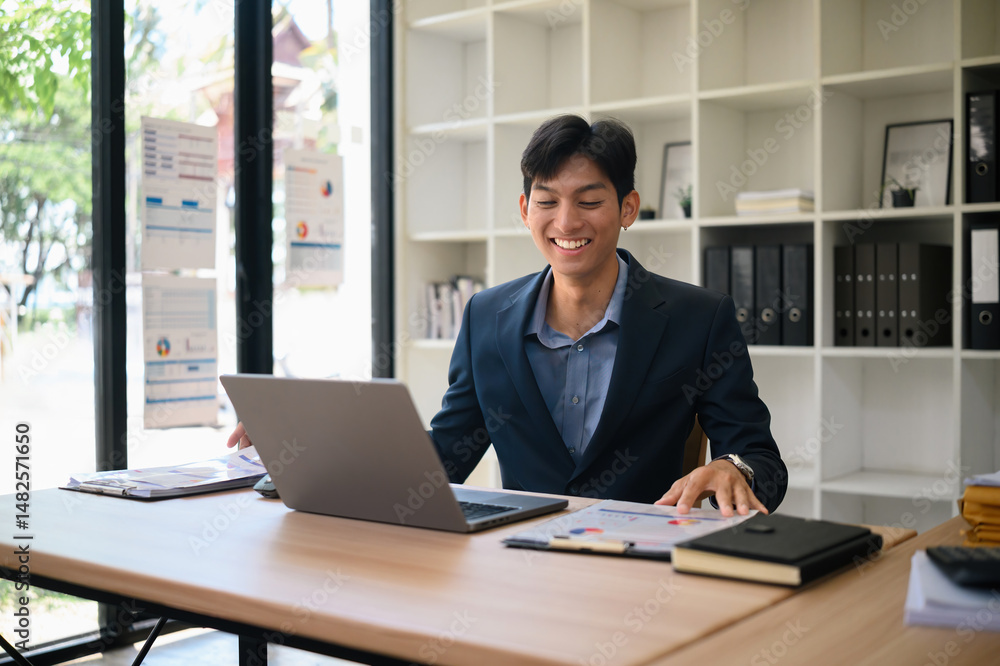 Confident Businessman Smiling While Working on Laptop at Office Desk Confident Businessman Smiling While Working on Laptop at Office Desk
