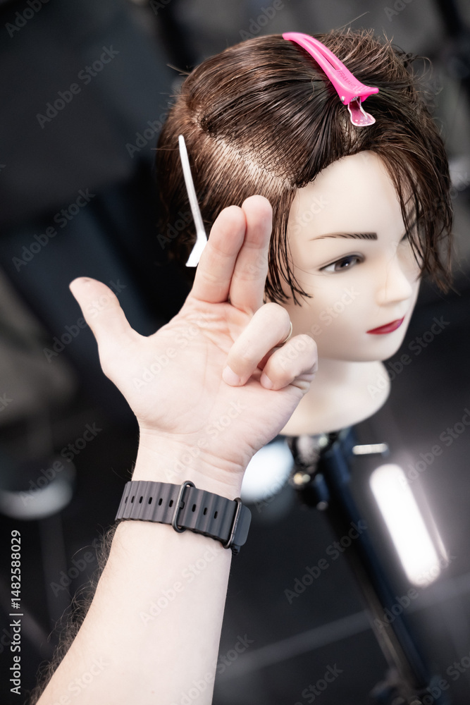 Fototapeta premium Close-up of student hands using scissors to cut synthetic hair on mannequin in beauty training session. Workshop