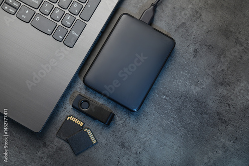 SD memory cards, USB flash drive, hard disk drive with cable and laptop on dark grey table, flat lay. Space for text