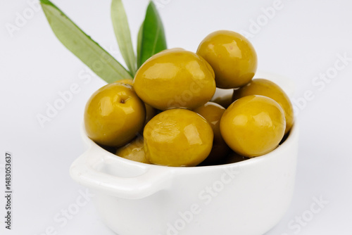 Minimal still life with green olives in bowl and olive twig on white background