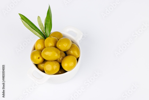 Organic olives in white bowl and olive twig on white tabletop background