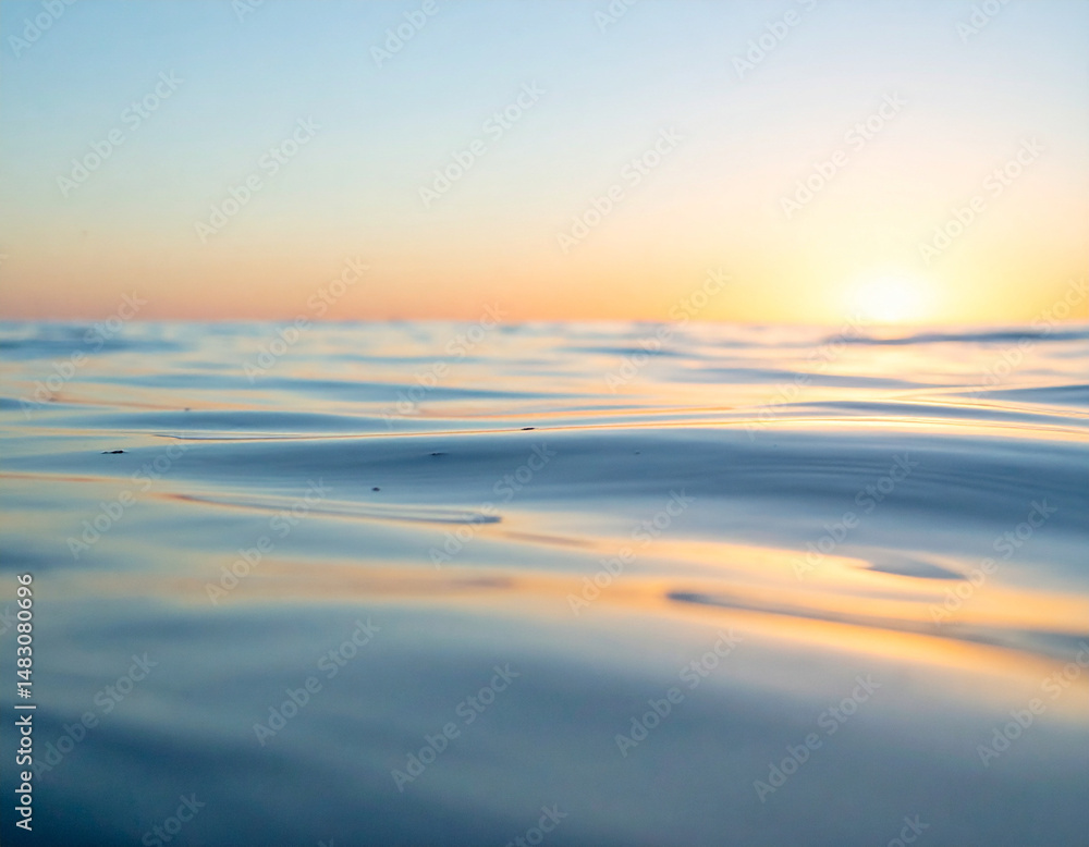 Obraz premium Gentle ripples of water reflecting soft orange sunlight under a pale blue sky.