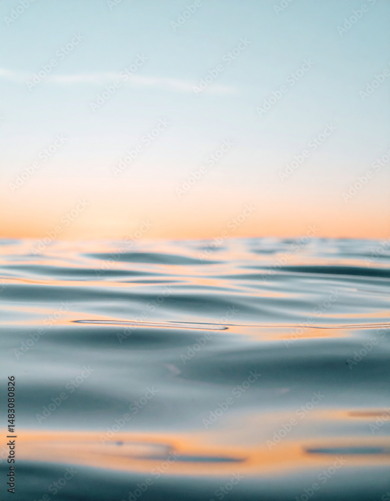 Fototapeta premium Gentle ripples of water reflecting soft orange sunlight under a pale blue sky.