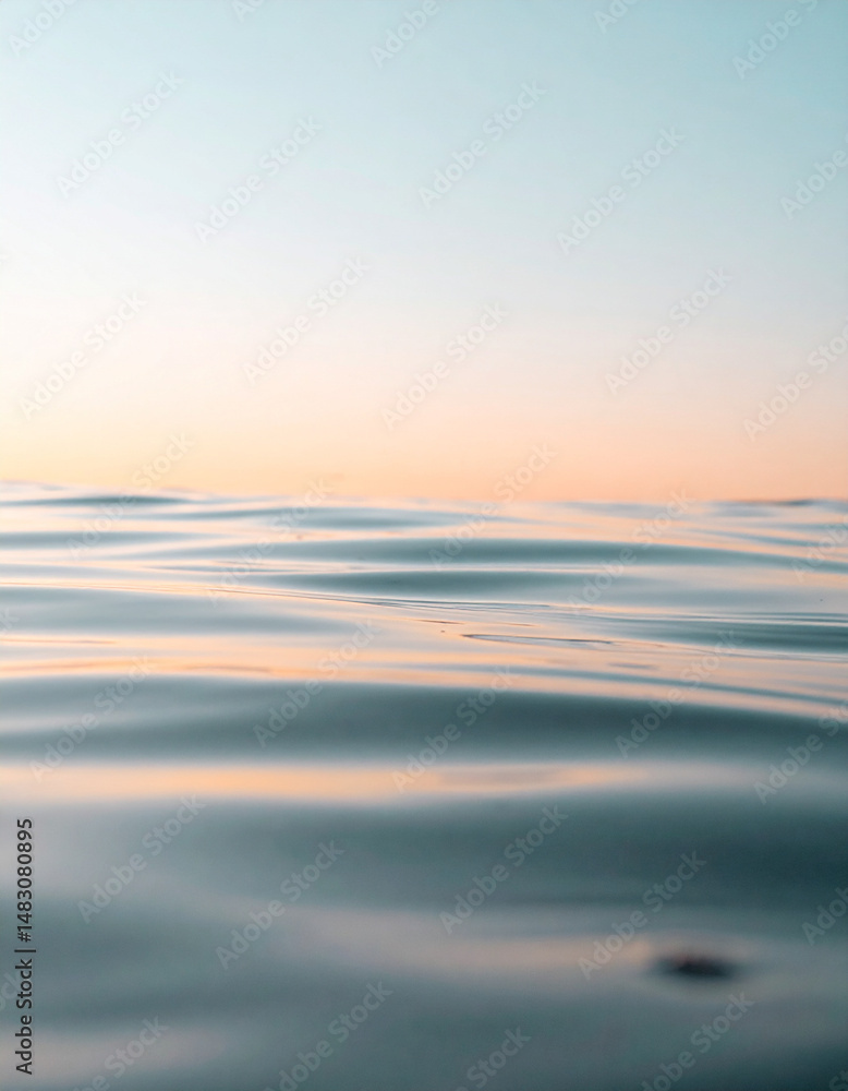 Fototapeta premium Gentle ripples of water reflecting soft orange sunlight under a pale blue sky.