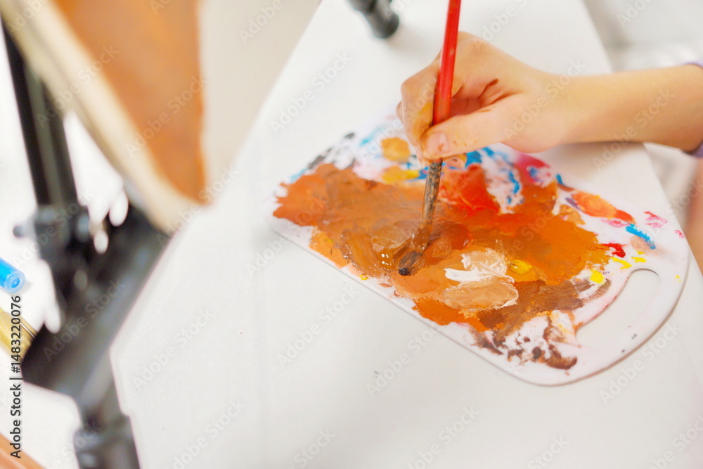 Fototapeta premium Close-up of a little girl hand mixing paint with a brush on a palette