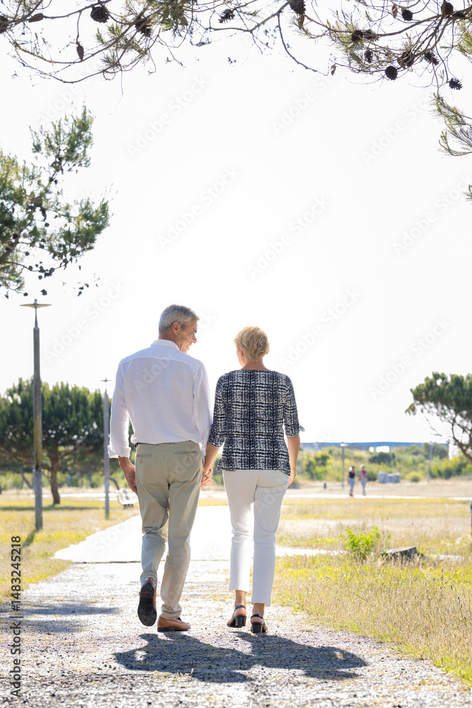 Senior couple walking in park holding hands on sunny day Senior couple walking in park holding hands on sunny day