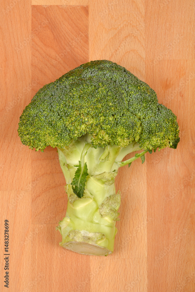 A single, fresh broccoli floret with a portion of its stalk rests on a light brown wooden surface