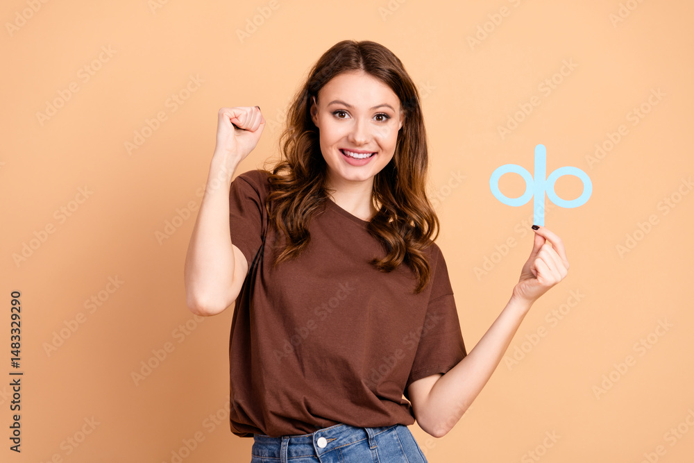 Happy woman in casual attire with brown shirt holding a blue symbol with confident gesture against beige background Happy woman in casual attire with brown shirt holding a blue symbol with confident gesture against beige background