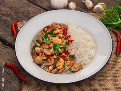 Rice topped with stir fried chicken and basil in white plate on wooden background. Thai Food