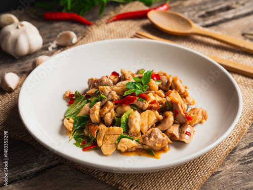 Stir fried chicken with basil and chili in white plate on wooden background. Thai Food
