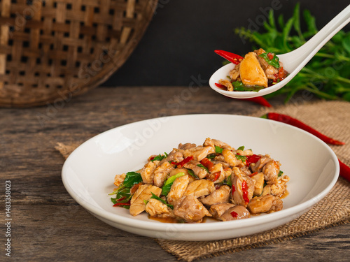 Use spoon to pick up stir fried chicken with basil and chili in white plate on wooden background. Thai Food
