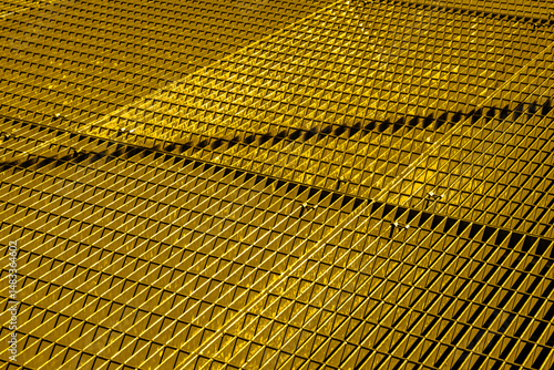 Gold metal grid, diagonal pattern. Interlaced bars create a geometric texture. Suitable for architecture, industry, or abstract design concepts.