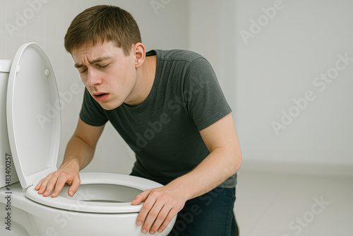 Young man feeling nauseous leaning over a toilet in a bathroom. Concept of food poisoning, illness, flu, or hangover.