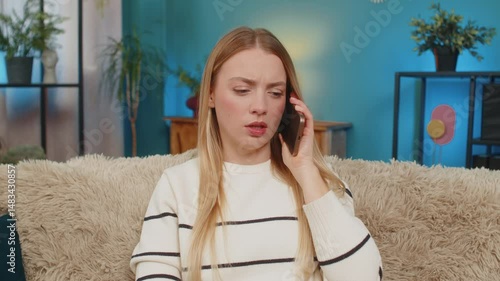 Caucasian young woman sitting on sofa at home feeling sadness and shock after receiving bad news on smartphone. Emotional girl holding phone to face, expressing empathy, still and thoughtful indoors